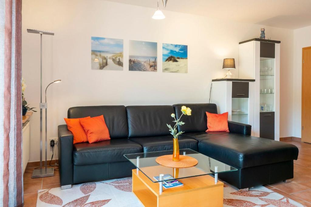 a living room with a black leather couch and orange pillows at Ferienpark Freesenbruch Wohnung 3 1 - Schöne Auszeit in Zingst