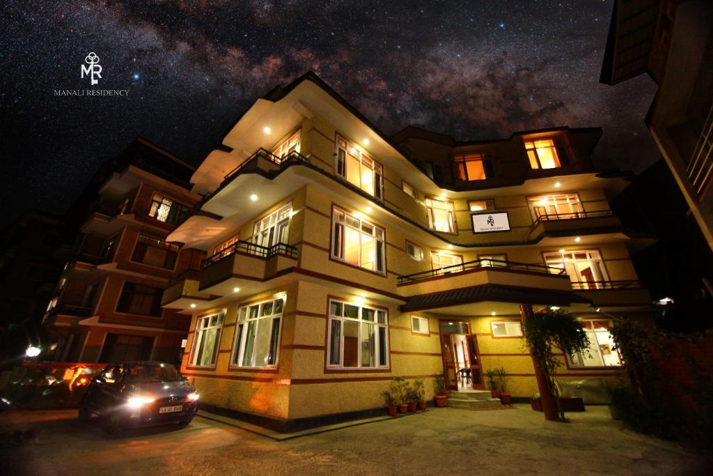 un bâtiment avec une voiture garée devant lui la nuit dans l'établissement Manali residency, à Manali