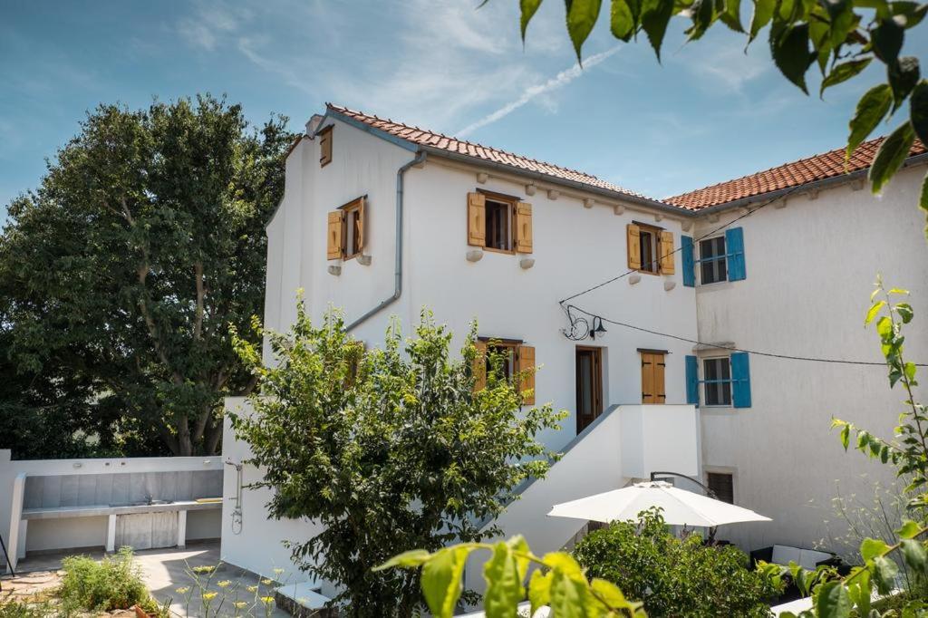 a white building with wooden windows and trees at Apartman STELLA MARIS in Veli Lošinj
