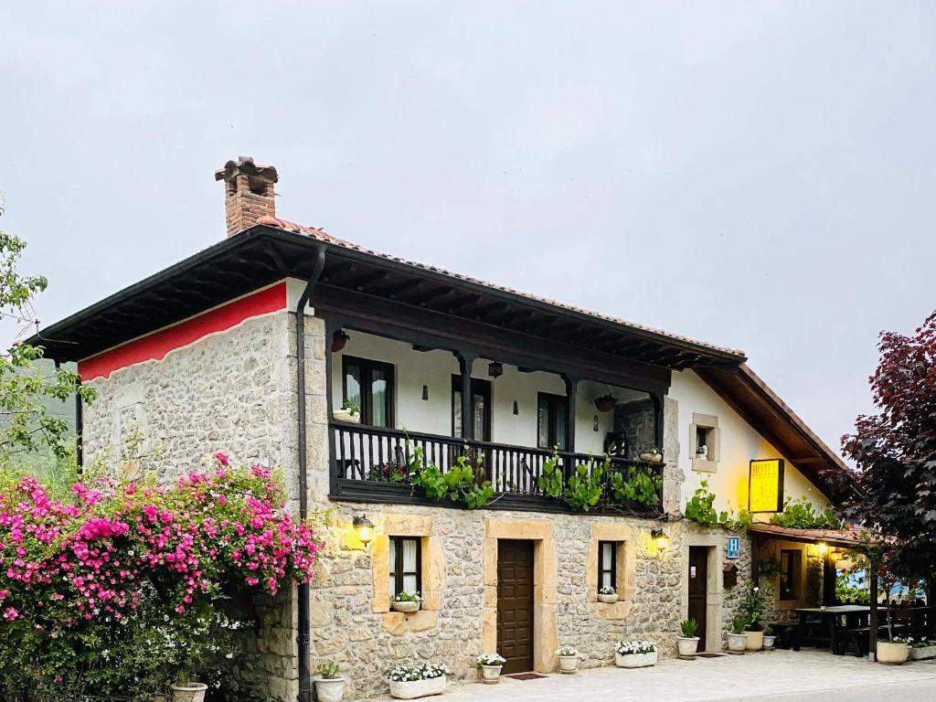 uma casa de pedra com uma varanda e flores cor-de-rosa em Hotel Alda em Avín