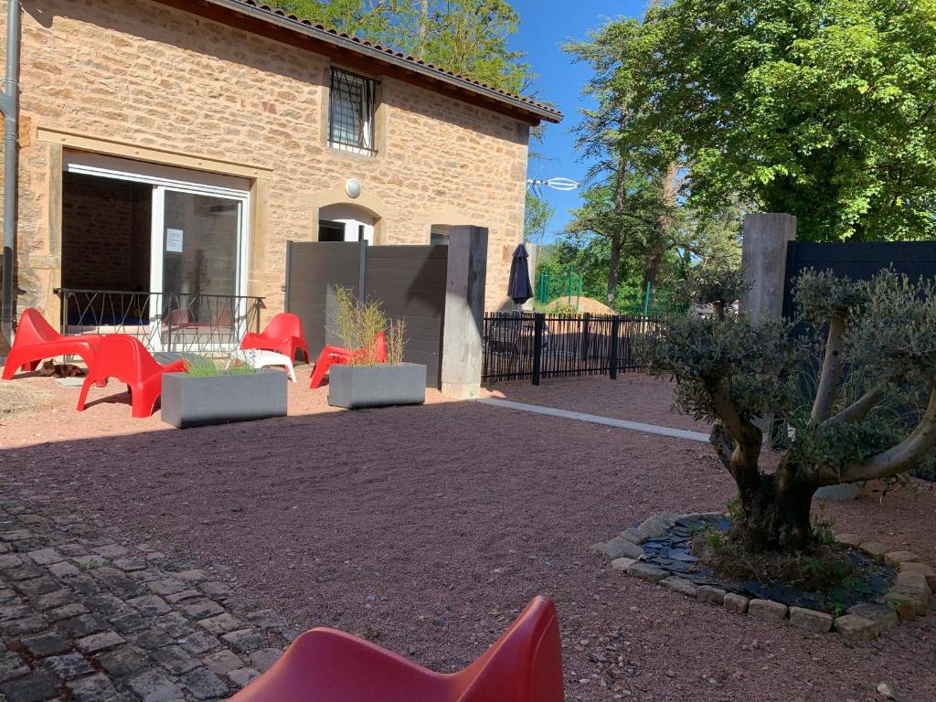 un patio con sillas rojas y un árbol frente a un edificio en La Maison Clémenso, en Cluny