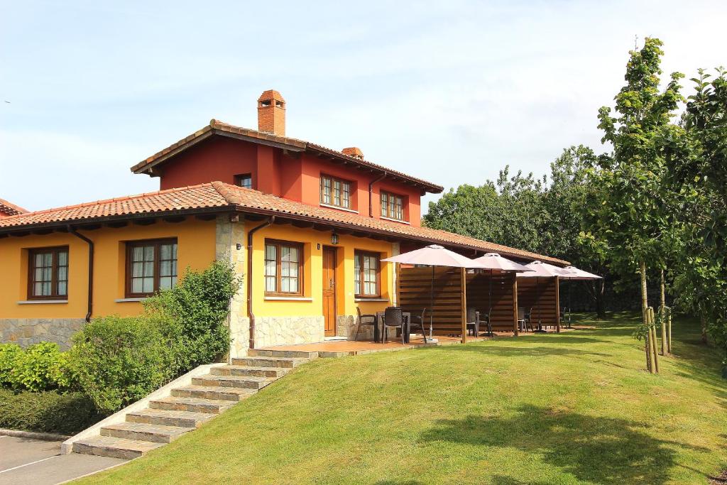 une maison jaune avec des tables et des parasols devant elle dans l'établissement Apartamentos Rurales Senda Costera, à Hontoria