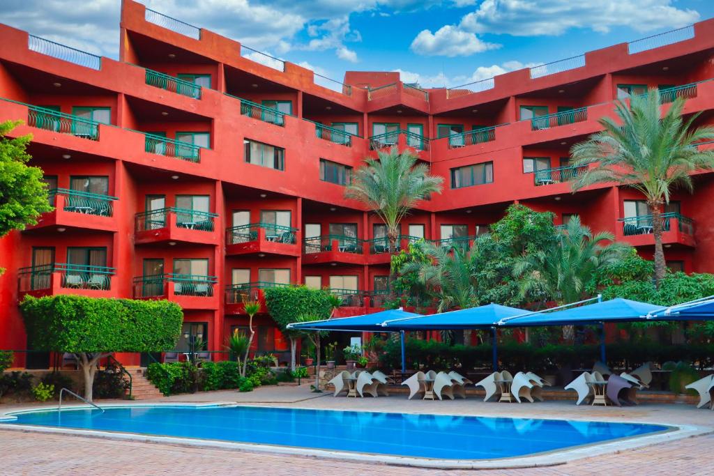 a red building with a pool in front of it at Adham Compound Hotel in King Mariout