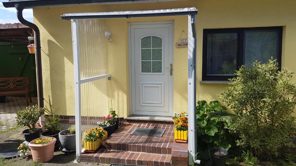 una casa amarilla con una puerta blanca y algunas plantas en Bungalow en Stralsund