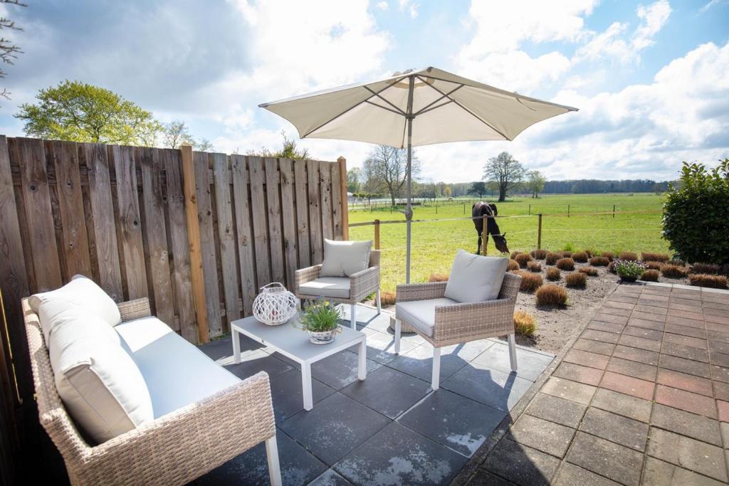 eine Terrasse mit einem Sonnenschirm, Stühlen und einem Tisch in der Unterkunft Vakantiehuis De Drie Bruggen in Valkenswaard