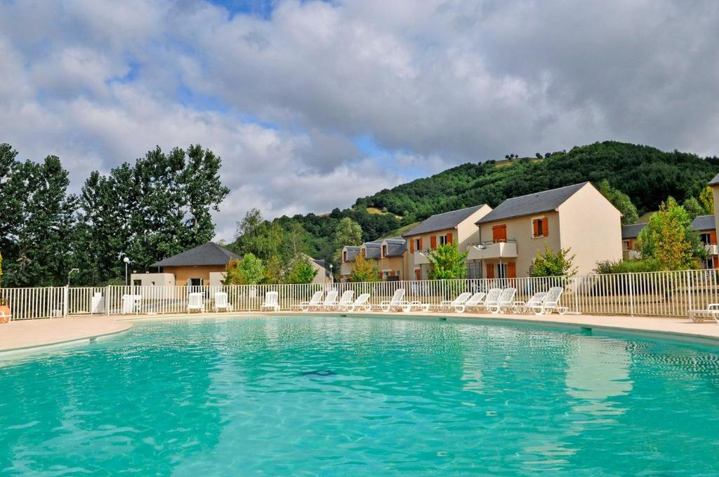 une grande piscine avec des chaises et une maison dans l'établissement T3 duplex village geolia Saint geniez d'olt avec 2 piscines aux portes de l'aubrac 64, à Saint-Geniez-dʼOlt