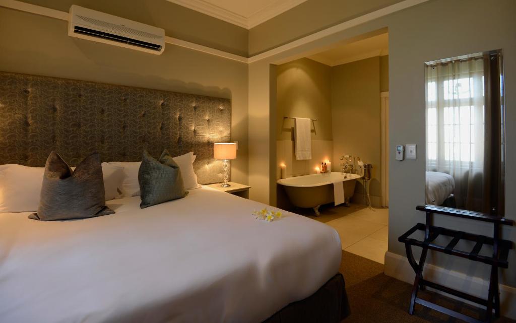 Cette chambre comprend un grand lit blanc et une baignoire. dans l'établissement Saint James on Venice, à Durban