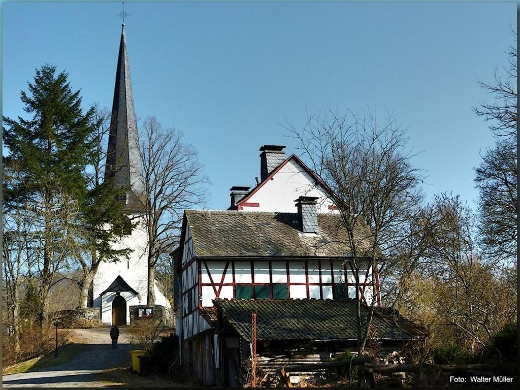 an old house and a church with a steeple at Alte Schule Kirmutscheid in Müsch