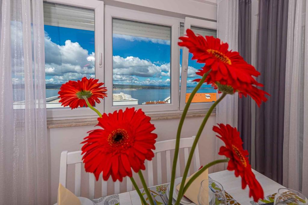 um vaso com flores vermelhas na frente de uma janela em Apartments in Crikvenica 41205 em Crikvenica