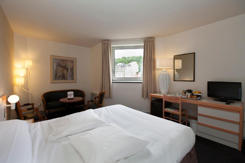 Habitación de hotel con cama, escritorio y TV. en Hôtel Paradis, en Lourdes