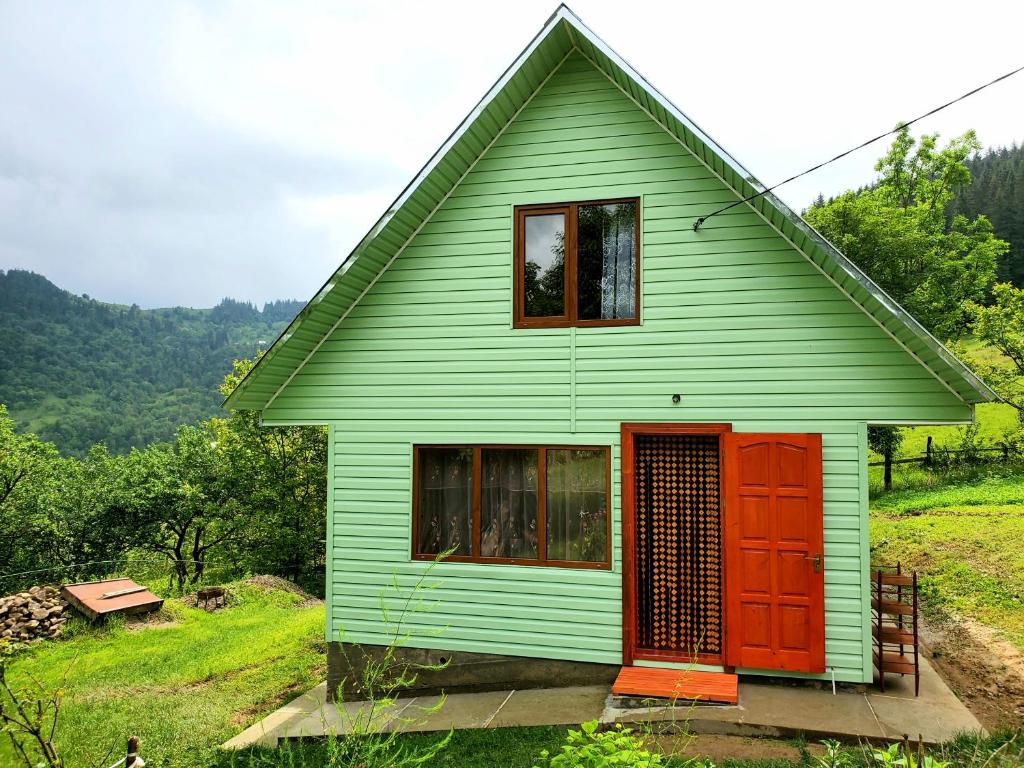 ein grünes Haus mit einer roten Tür auf einem Hügel in der Unterkunft Садиба Кичера in Petrashani