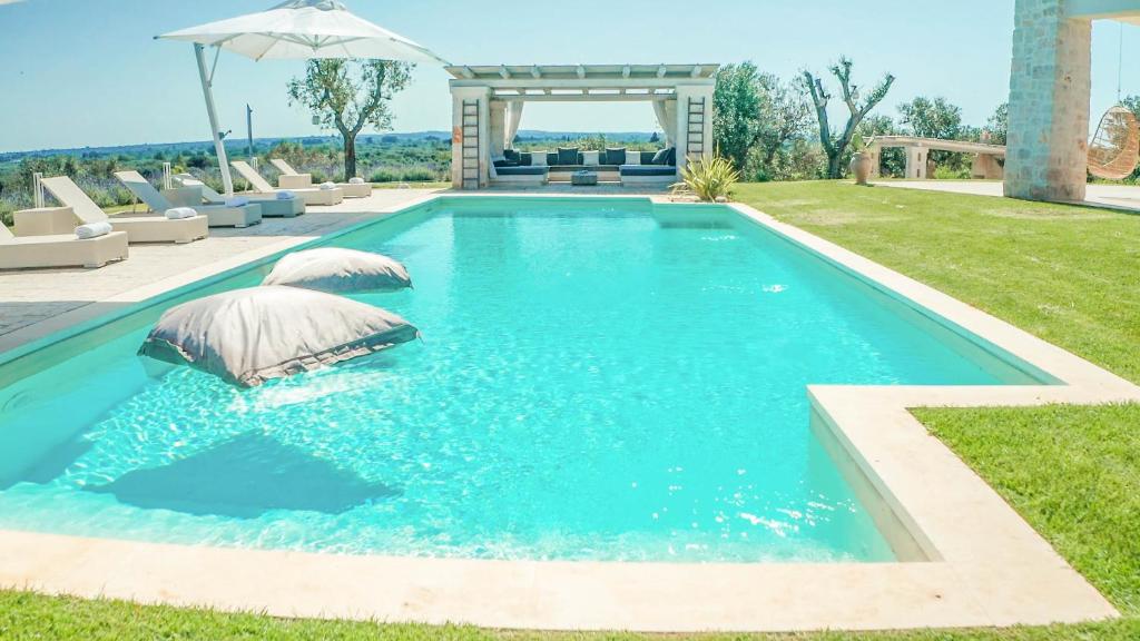 een zwembad in een tuin met stoelen en een parasol bij Tenuta Lamia degli Ulivi - Ostuni Puglia - Ancient Lamia and Modern Villa in Ostuni