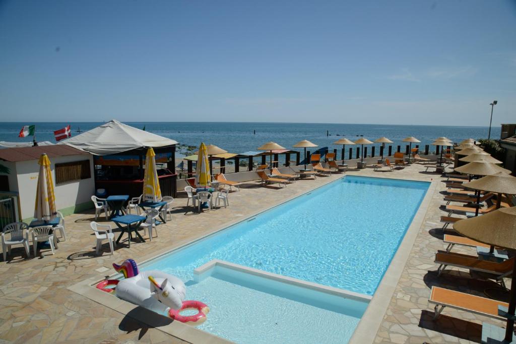 una piscina con sillas y sombrillas y el océano en Residence Baiadosol en Lido di Fermo