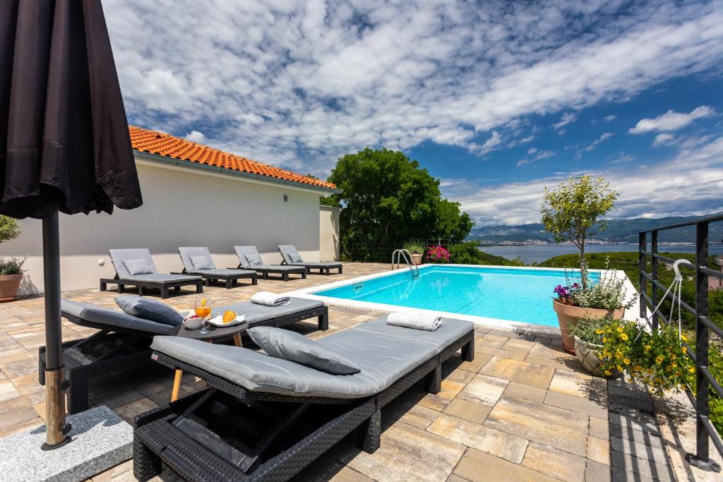 a swimming pool with a patio furniture and an umbrella at Apartment MAGAŠ in Vrbnik