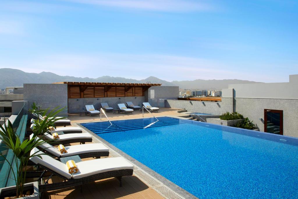 a pool on the roof of a building with lounge chairs at Royal Tulip Muscat in Muscat