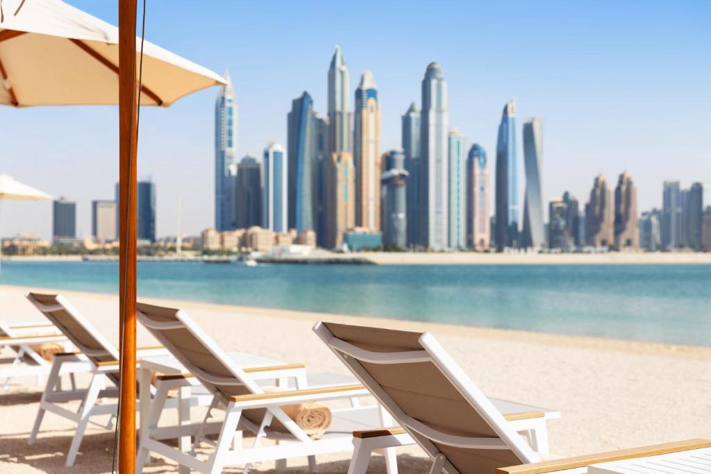 una fila di sedie a sdraio su una spiaggia con una città di Adagio Premium The Palm a Dubai