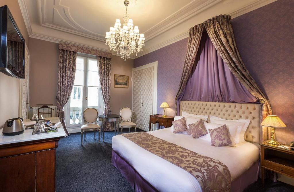 um quarto de hotel com uma cama e um lustre em Hotel Claridge Paris em Paris