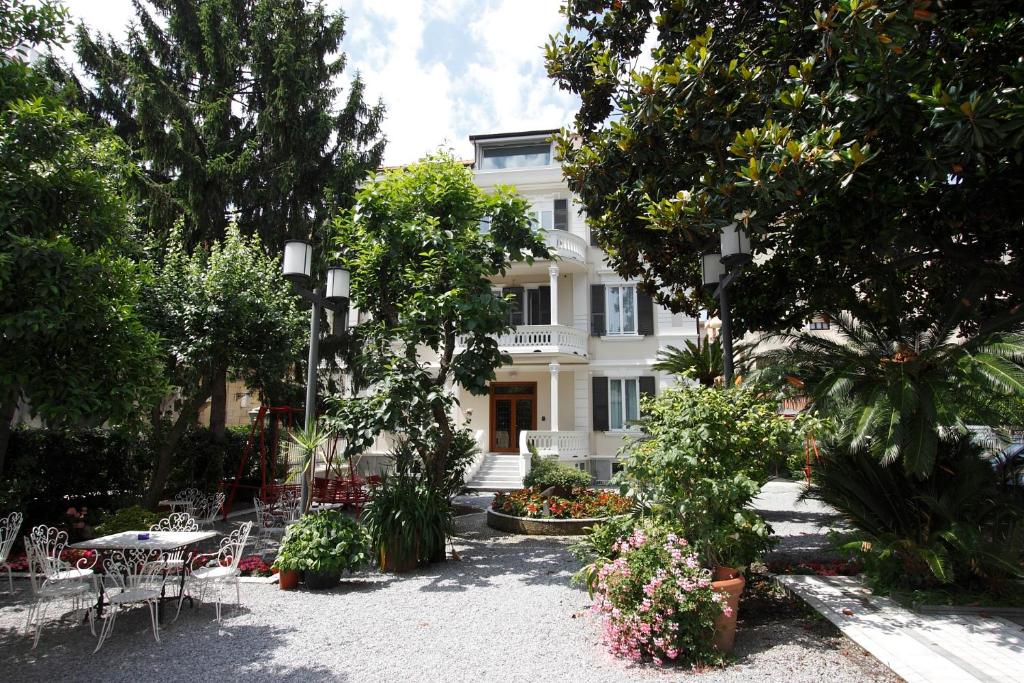 una casa bianca con tavoli, sedie e alberi di Genovese Villa Elena Residence a Varazze