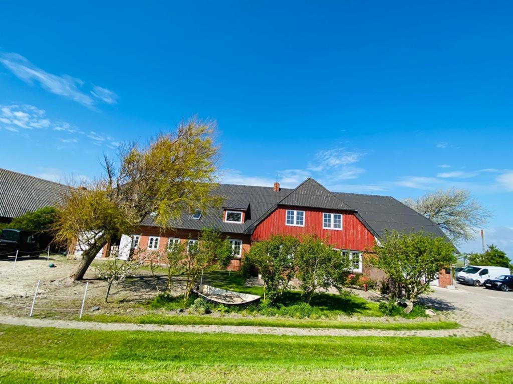 a large red house with a yard with trees at HaRe Ferienwohnungen in Langeneß