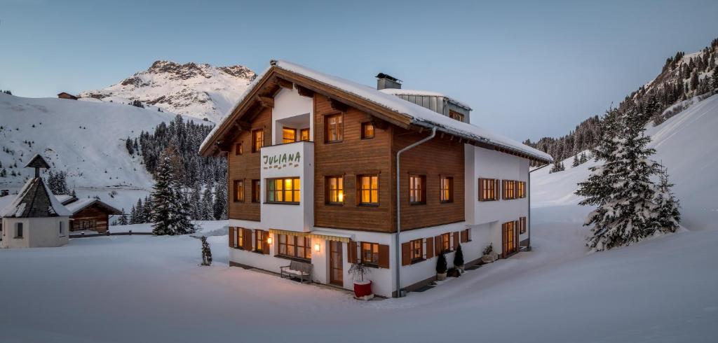 a large wooden house in the snow with a mountain at Pension Juliana in Lech am Arlberg