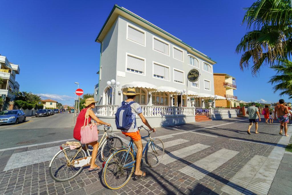 due persone che pedalano in bicicletta lungo una strada di fronte a un edificio di Hotel Il Settebello a Marina di Cecina