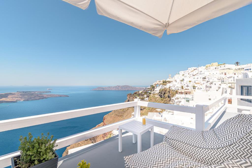 Un balcón con sillas blancas y vistas al océano. en Avianto Suites, en Imerovigli