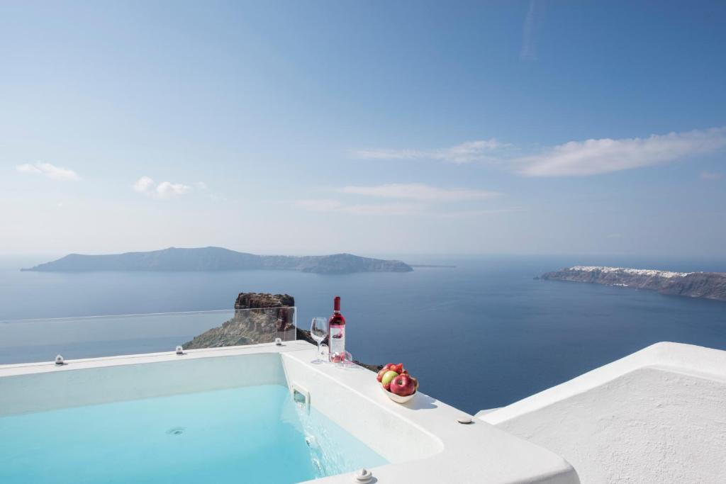 a bottle of wine and fruit sitting on a ledge overlooking the ocean at Elia Cave Suites in Imerovigli