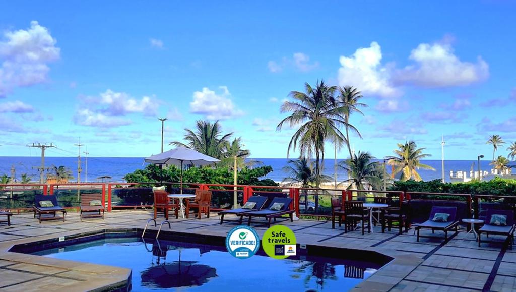 einen Pool mit Stühlen, Tischen und Meerblick in der Unterkunft Bahiamar Hotel in Salvador