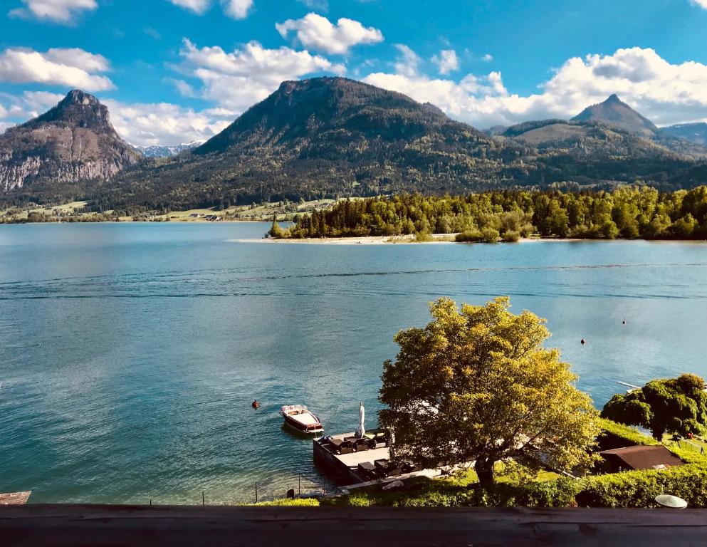 a boat on a lake with mountains in the background at Strandhotel Margaretha in St. Wolfgang