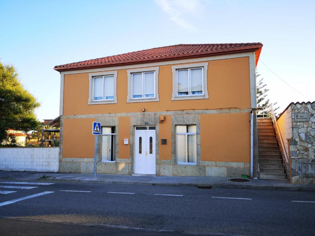 une maison orange avec une porte blanche dans une rue dans l'établissement Piso da Horta en Aguiño, Ribeira, Galicia, à Ribeira