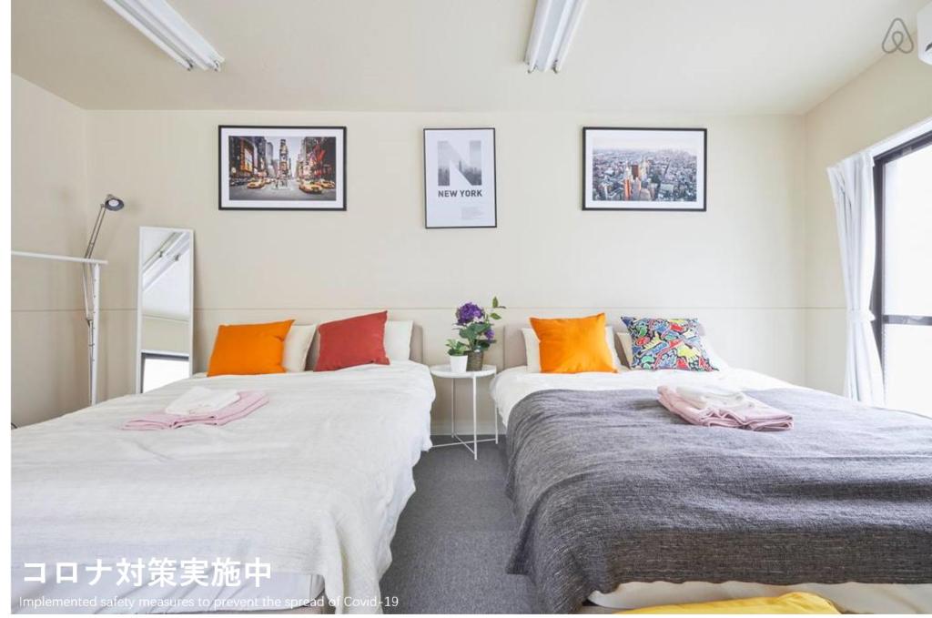 2 Betten in einem Zimmer mit orangefarbenen Kissen in der Unterkunft TORA HOTEL Tokyo-kitaueno 寅ホテル北上野 in Tokio