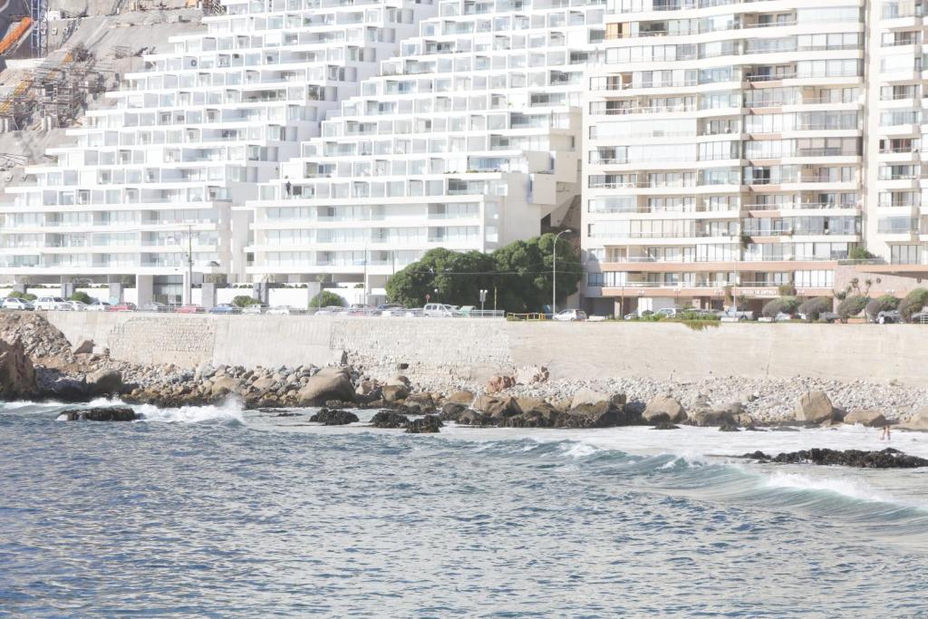 un grupo de rocas en la playa con un gran edificio en Resetéate frente al Mar!! Disfruta en primera línea de Cochoa-Reñaca, en Viña del Mar