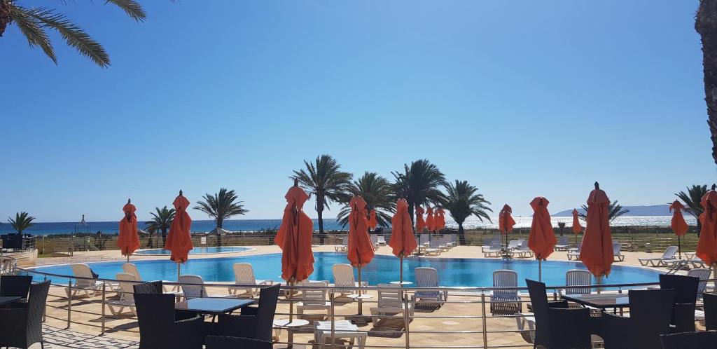 uma piscina com guarda-sóis e cadeiras vermelhas e o oceano em Andalucia appart hoteL em Bizerte