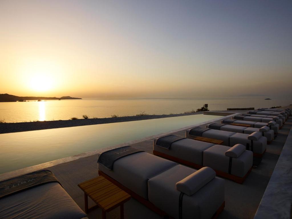 a row of chaise lounges next to a swimming pool with the sunset at Domes White Coast Milos, Adults Only - Small Luxury Hotels of the World in Mytakas