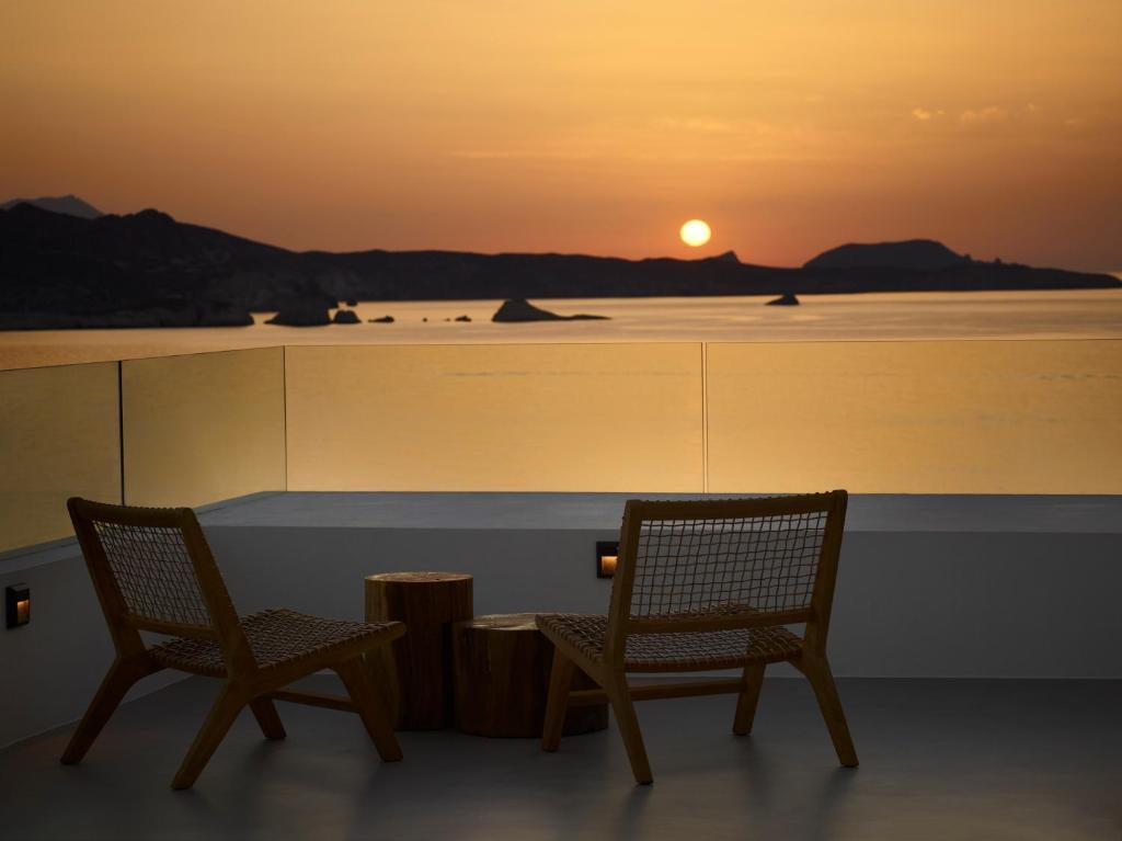 two chairs and a table with a sunset in the background at Domes White Coast Milos, Adults Only - Small Luxury Hotels of the World in Mytakas