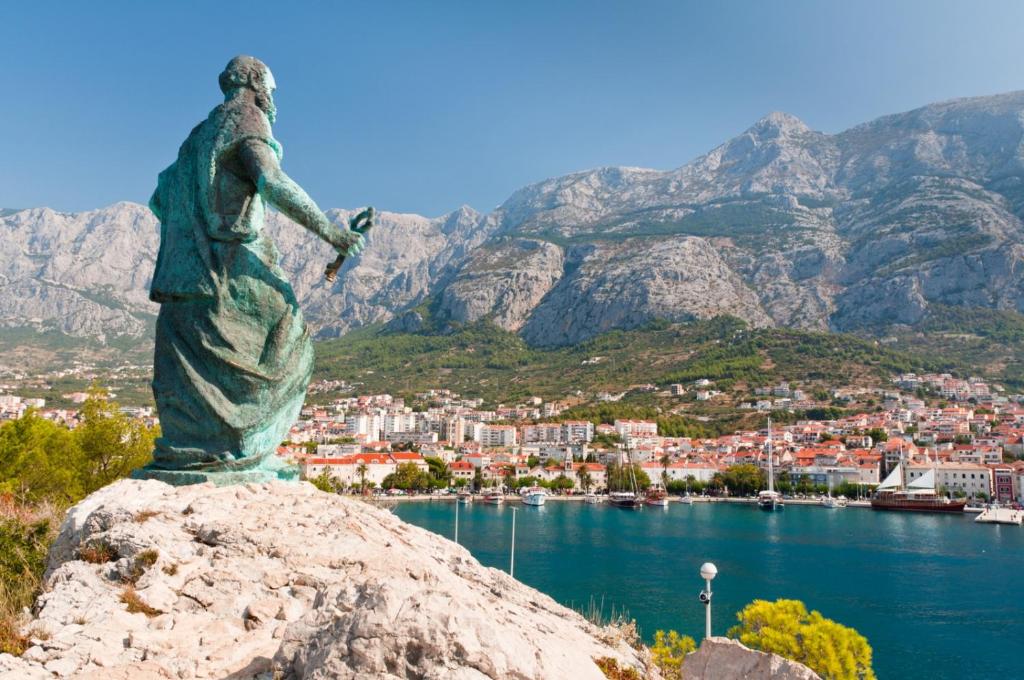 une statue d'une femme debout sur un rocher surplombant une ville dans l'établissement Beachfront Apartment Podgora (205-2), à Podgora