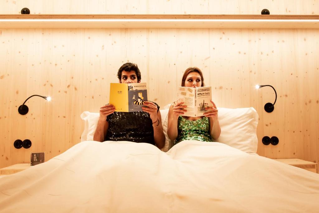 a woman sitting on a bed with a book at Zero Box Lodge Porto in Porto
