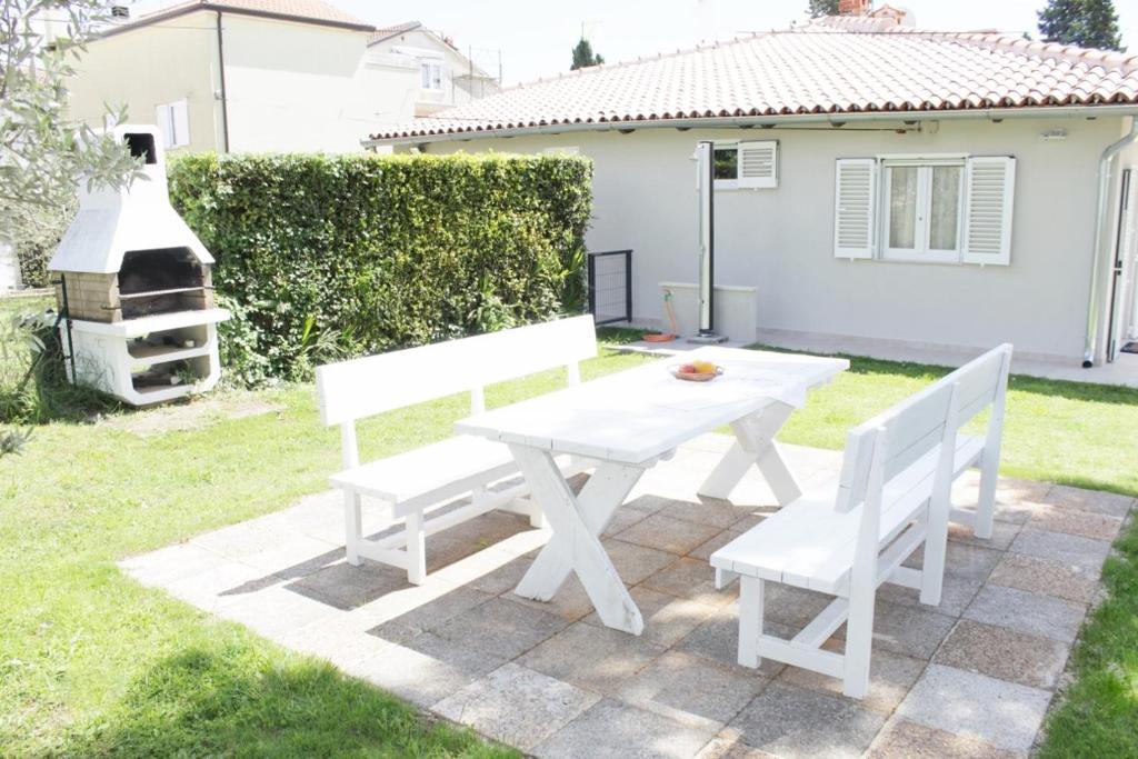 a white picnic table and two white chairs in a yard at Holiday house PUNTA Umag II in Umag