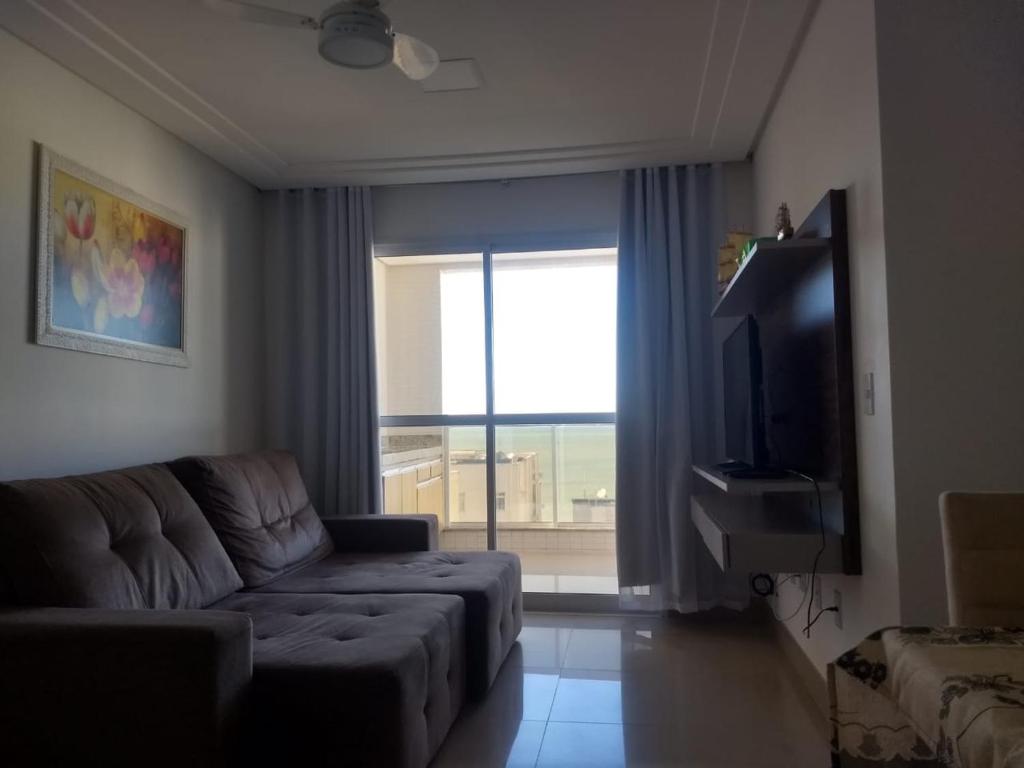 un salon avec un canapé et une grande fenêtre dans l'établissement Edifício Gil Nogueira, apartamento aconchegantes, piscina, sauna, Wiff, duas vagas de garagem., à Guarapari