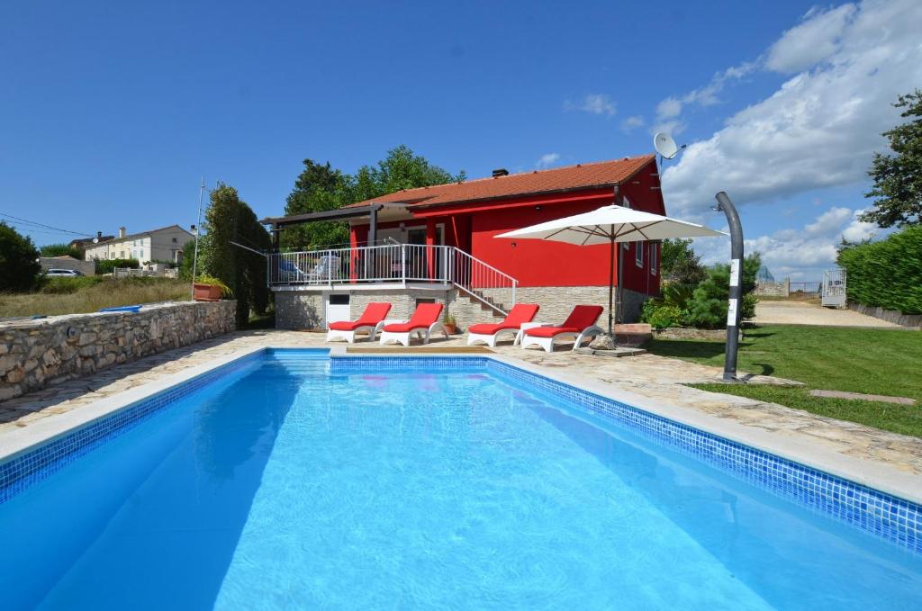 a swimming pool with two chairs and a red house at Villa Ketty in Kanfanar