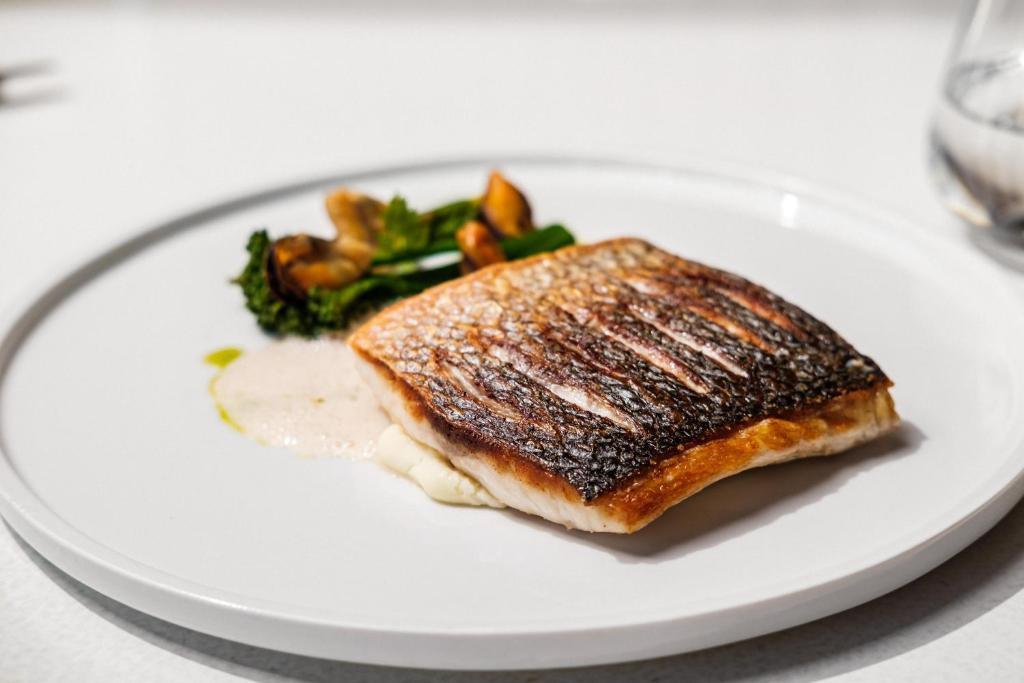 a white plate with a piece of fish and vegetables at Hyatt Regency Malta in St. Julianʼs