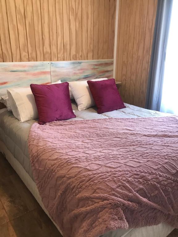 a bed with purple and white pillows on it at Apart Hotel Don Domingo Coñaripe in Coñaripe