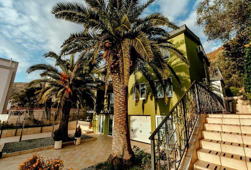 two palm trees in front of a yellow building at Olive Garden Apartment in Petrovac na Moru