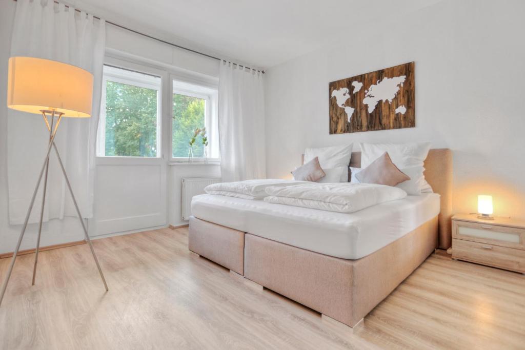 a white bedroom with a large bed and a lamp at JUNIK Apartments "Am Sternbuschweg" in Duisburg