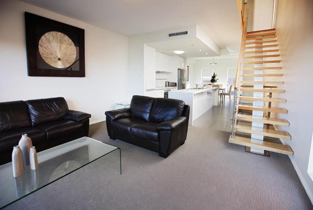 a living room with black leather furniture and a staircase at Charlestown Executive Apartments in Newcastle