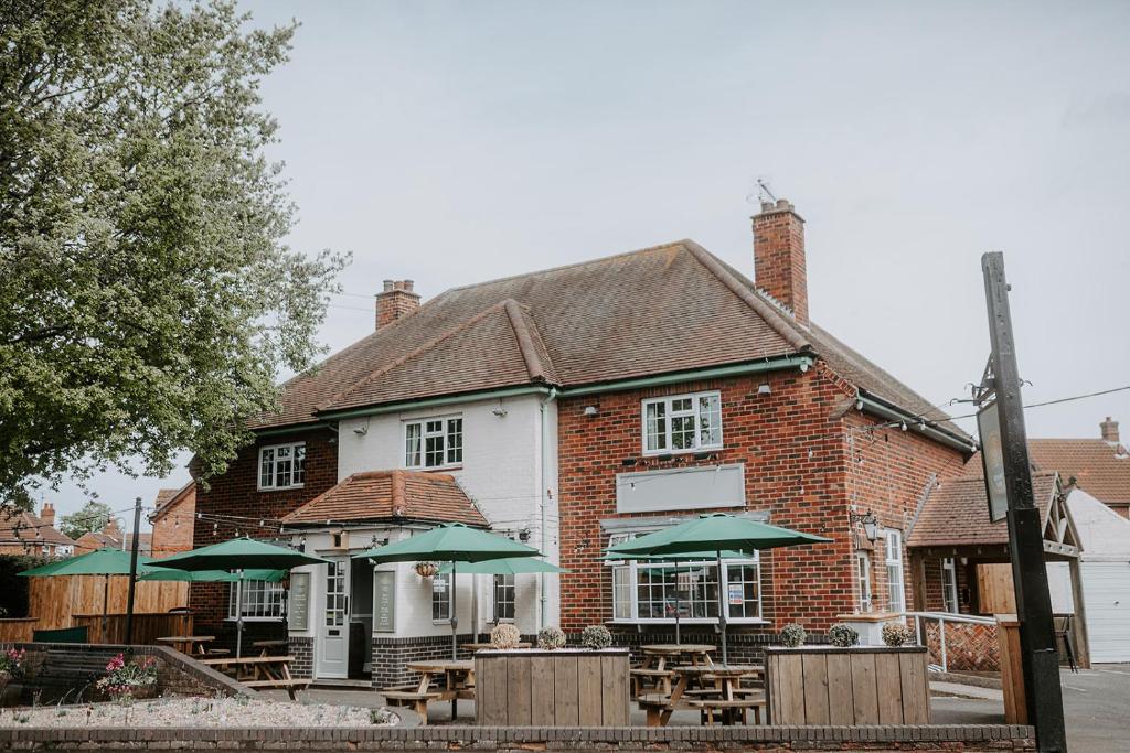 un edificio de ladrillo con mesas y sombrillas verdes en The Royal Oak, en Heckington