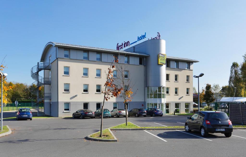 un bâtiment avec une voiture garée sur un parking dans l'établissement First Inn Hotel Paris Sud Les Ulis, aux Ulis