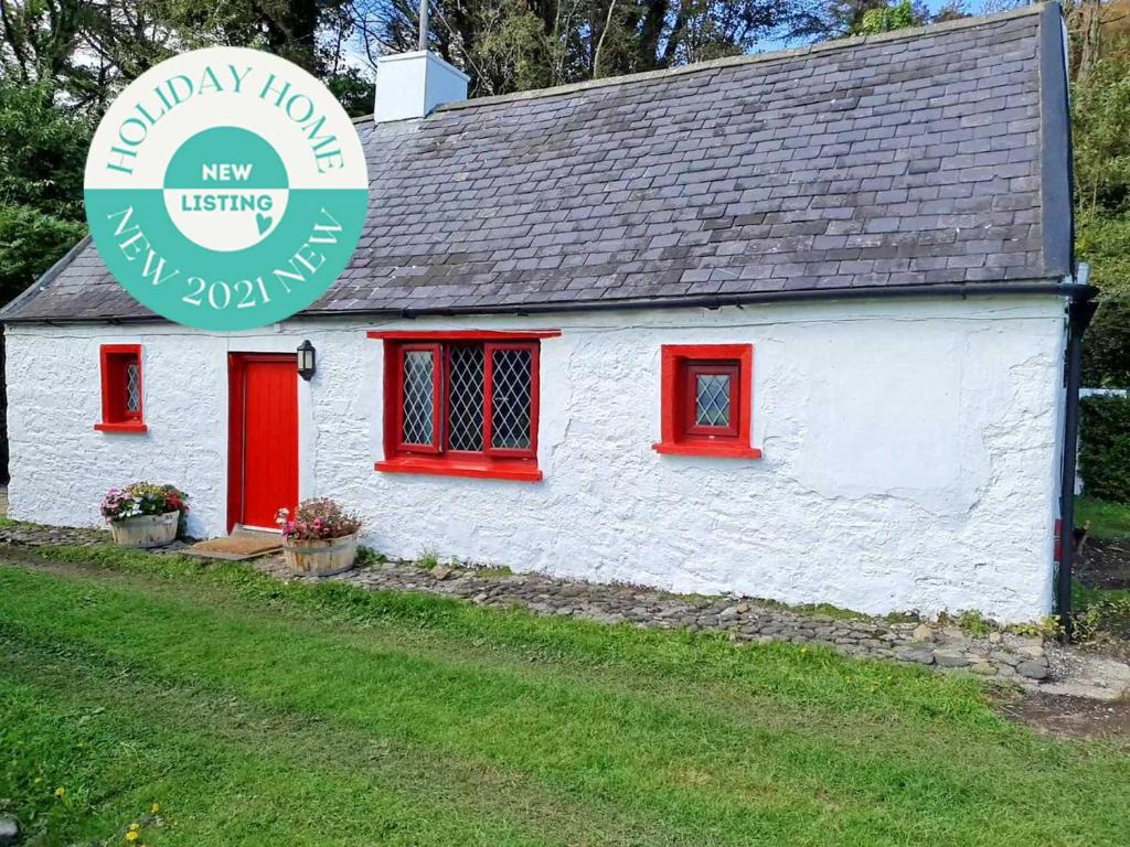 Cabaña blanca con ventanas rojas y un cartel en Wreckers Cottage en Dunmore East