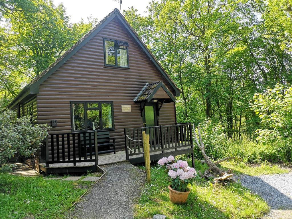 a cabin in the woods with a porch and flowers at PrancingHare Lodge-Woodland Lodges-Pembrokshire in Carmarthen