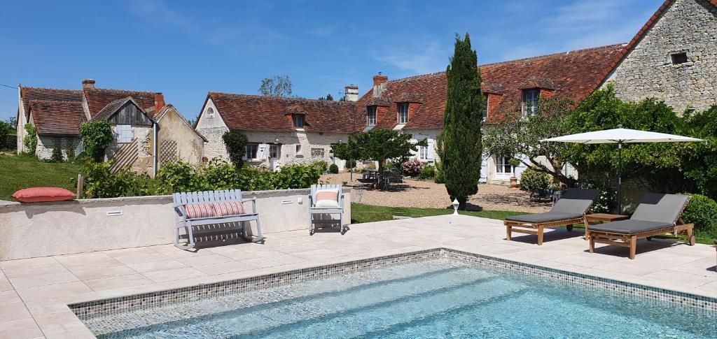 una piscina con sillas y una sombrilla junto a una casa en La Ferme Blanche en Cussay